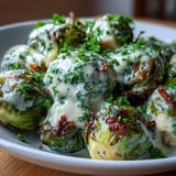 Tender Brussels sprouts coated in a creamy, tangy sauce with garlic and onion, served warm as a savory vegetarian side dish.
