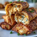 Twelve Buffalo Chicken Dip Egg Rolls on a platter, melty cheddar and green onions visible in the torn wrapper.