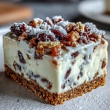 A close-up slice of Christmas Cheesecake Slab reveals dried fruits in a velvety, spiced cream cheese filling.