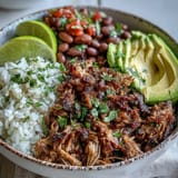 Slow-cooked carnitas bowl featuring pinto beans, lime wedges, and vibrant pico de gallo for a hearty Mexican-inspired meal.