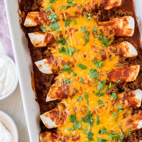 Freshly baked Beef Enchiladas served with a dollop of sour cream and a side of rice for a complete meal.  