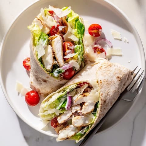 Freshly assembled Chicken Caesar Wrap halved to reveal shaved Parmesan and juicy tomato halves on a wooden board.  