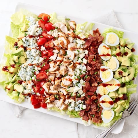 Cobb salad recipe featuring rows of vibrant ingredients, including ripe tomatoes, blue cheese, and a tangy red wine dressing.