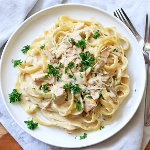 Steaming fettuccine Alfredo pasta coated in a rich butter and Parmesan sauce, served in a white bowl.