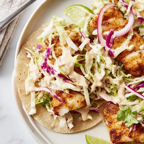 A close-up of grilled white fish tacos topped with chopped cilantro, red onion slices, and fresh lime wedges on a rustic wooden board.