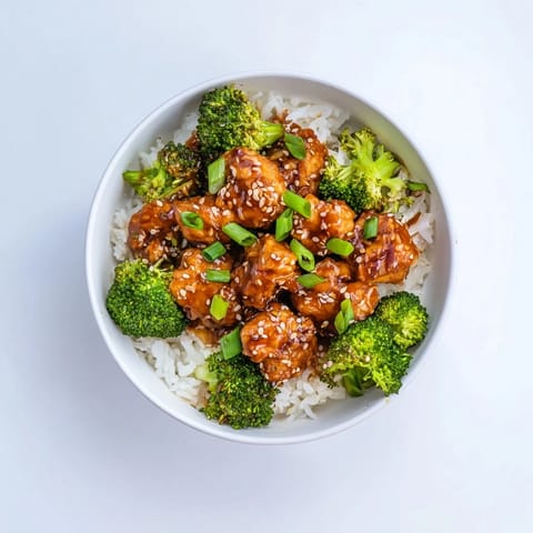Sweet chili chicken bowl garnished with fresh green onions and sesame seeds on a rustic table.  