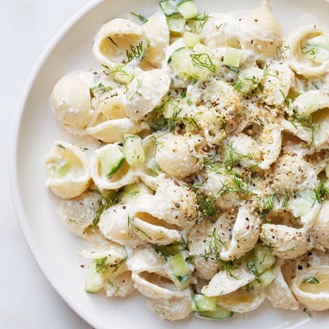 Creamy Cucumber Crunch Pasta Salad in a white bowl, featuring shell pasta, diced cucumbers, and fresh dill on a rustic wooden table.  