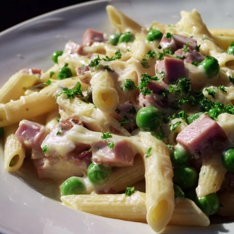 Close-up of creamy Spring Pea & Ham Pasta with tender penne, sweet green peas, and savory diced ham glistening in a rich sauce.