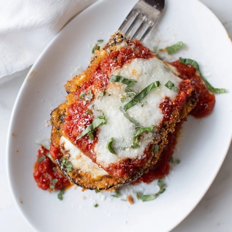 A close-up of homemade Eggplant Parmesan topped with fresh basil, served alongside a crisp green salad.