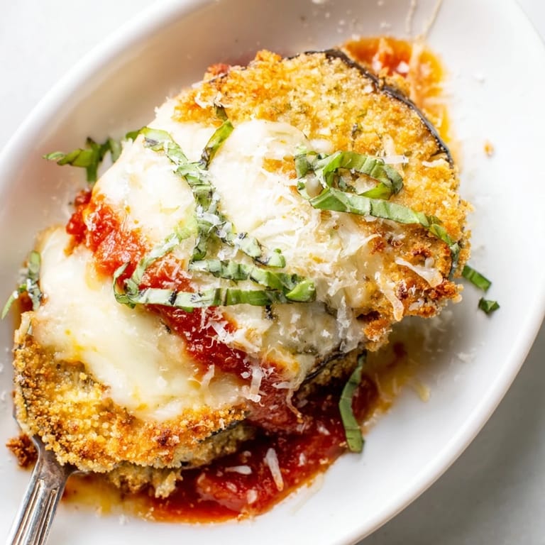 Serving plate of bubbling Eggplant Parmesan with layers of crispy breaded eggplant, tomato sauce, and Parmesan.