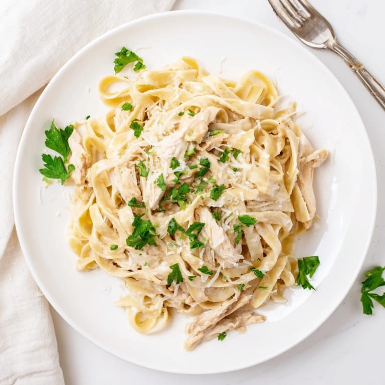 A plate of homemade fettuccine Alfredo with golden sautéed chicken and a sprinkle of extra grated Parmesan.