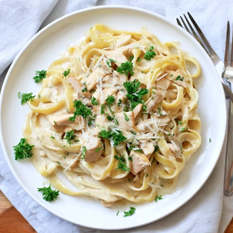 Steaming fettuccine Alfredo pasta coated in a rich butter and Parmesan sauce, served in a white bowl.