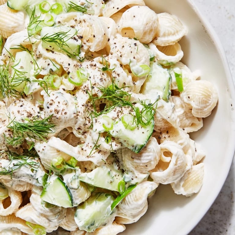Vibrant bowl of Cucumber Crunch Pasta Salad with tender shells, crisp cucumber pieces, and a sprinkle of seasoning garnish.