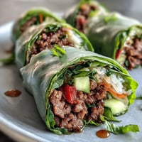 Golden Thai Basil Beef Rolls stuffed with ground beef, crisp veggies, and fresh herbs, resting on a white platter. 